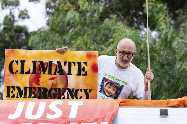 Nat Tunbridge on top of the oil tanker with a photo of his son on his t-shirt and holding a Climate Emergency sign. Photo Matt Hrkac.